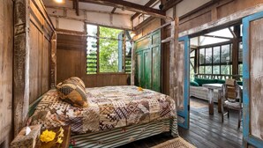 A rustic bedroom with a large bed, wooden walls, and a view of greenery outside. - Singing River Front Villa (Tabanan)