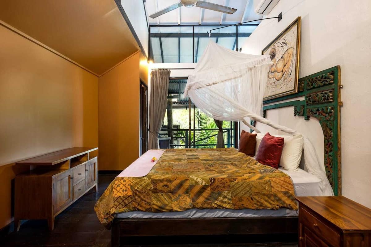 A bedroom with a bed, a wooden nightstand, a bench, and a ceiling fan.