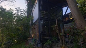 A modern building with a glass facade, surrounded by lush greenery and stone pathways. - Singing River Front Villa (Tabanan)