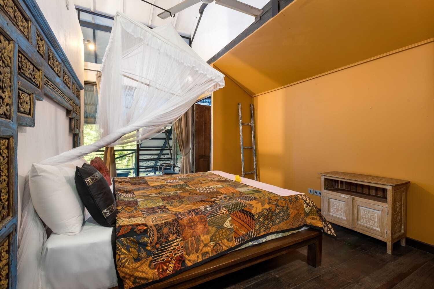 A bedroom with a bed, a wooden nightstand, a white canopy bedspread, and a patterned rug.