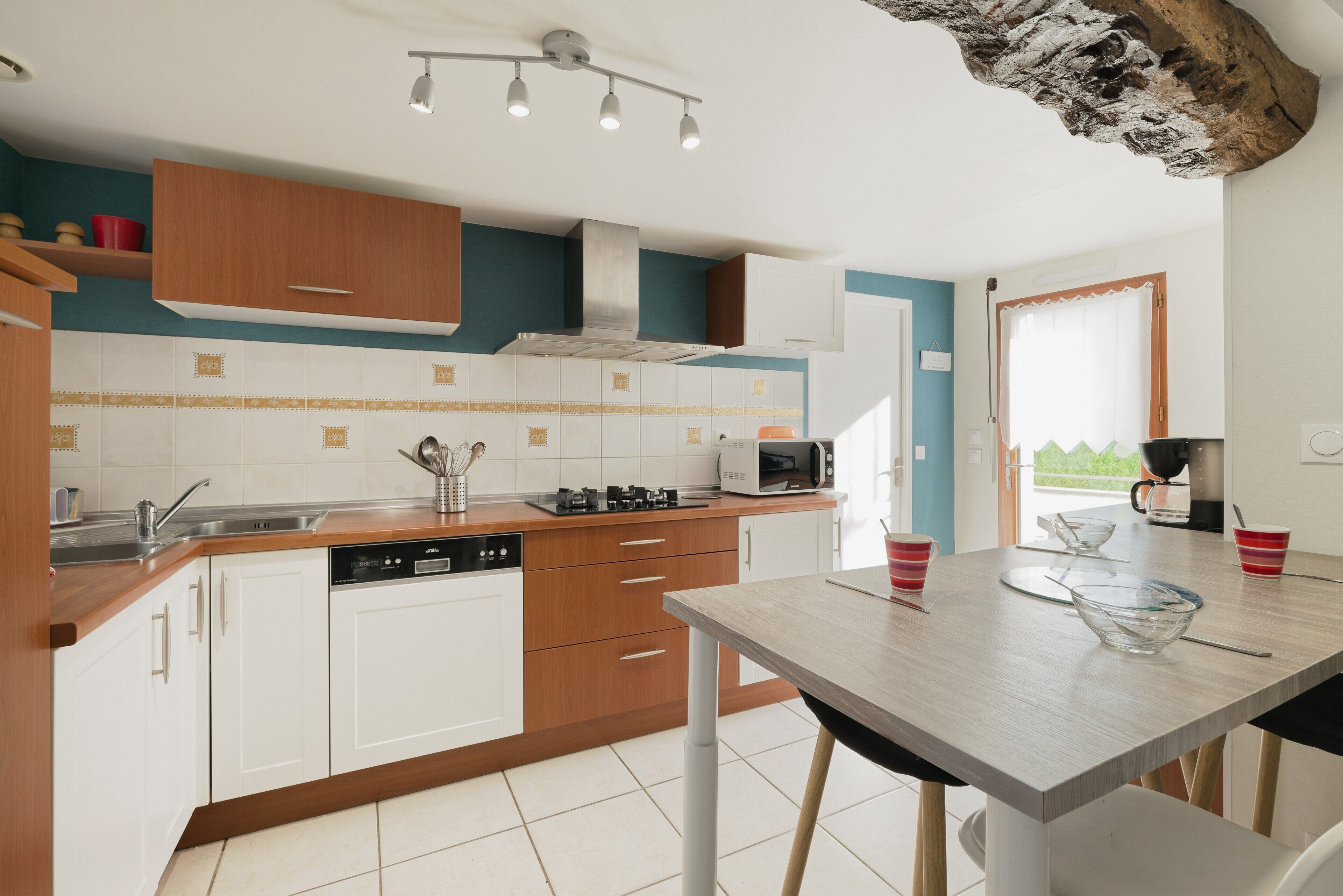 Een moderne keuken met witte kastjes, een houten aanrecht, een vaatwasser, een magnetron en een koffieapparaat.