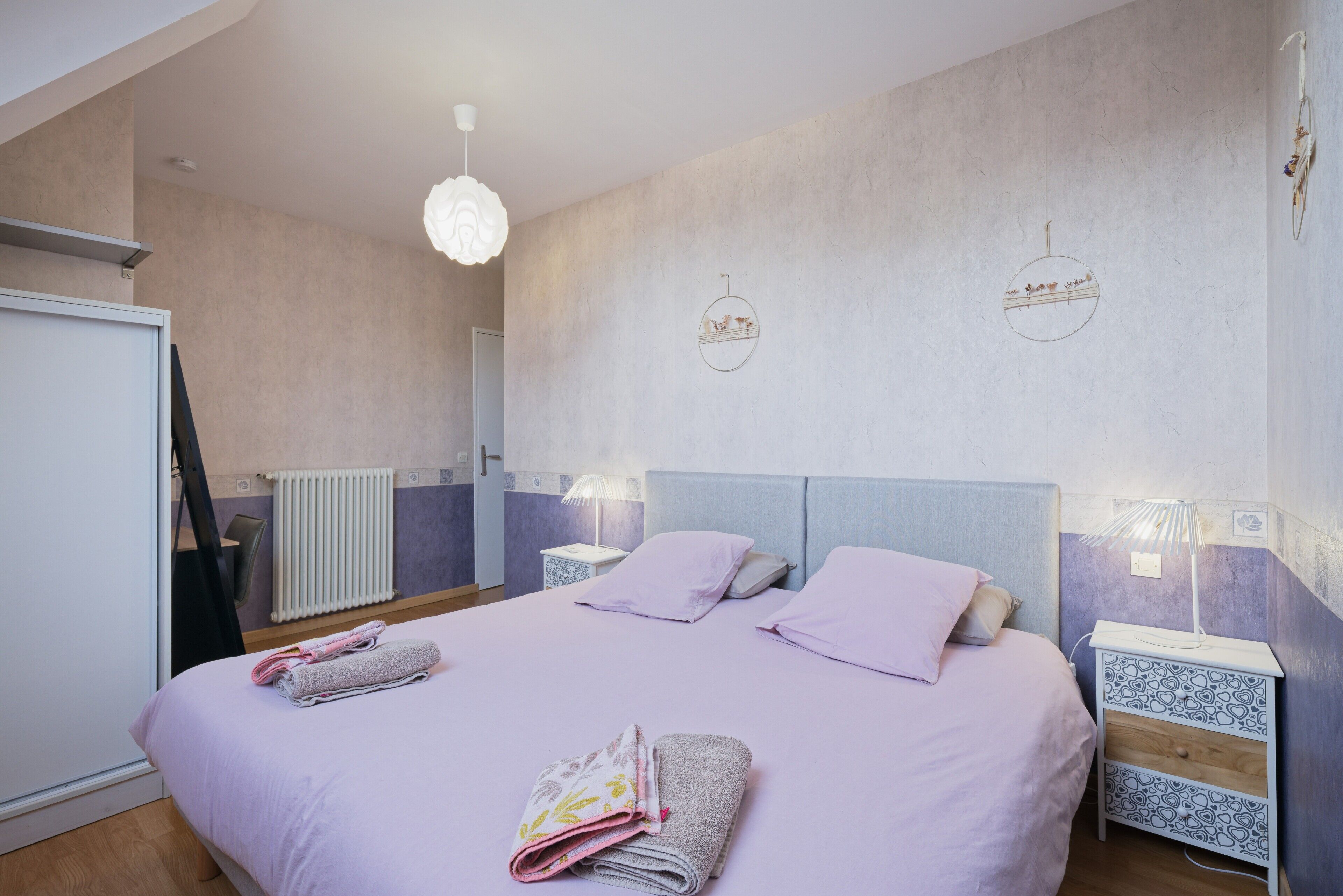 Un dormitorio con una cama, dos mesitas de noche, un radiador y una lámpara colgante.