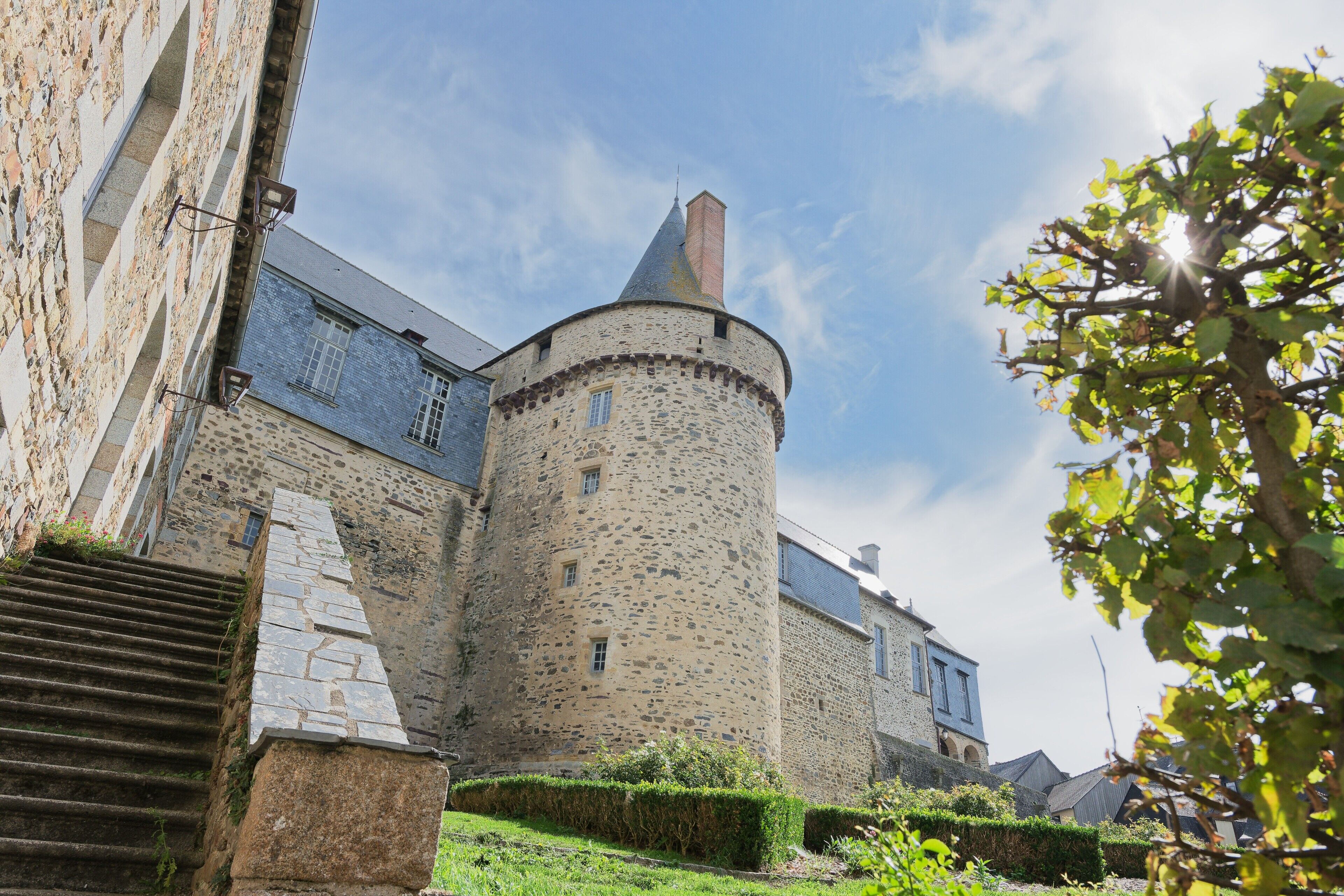 Un château en pierre doté d’une tour ronde, d’un escalier et d’une haie.
