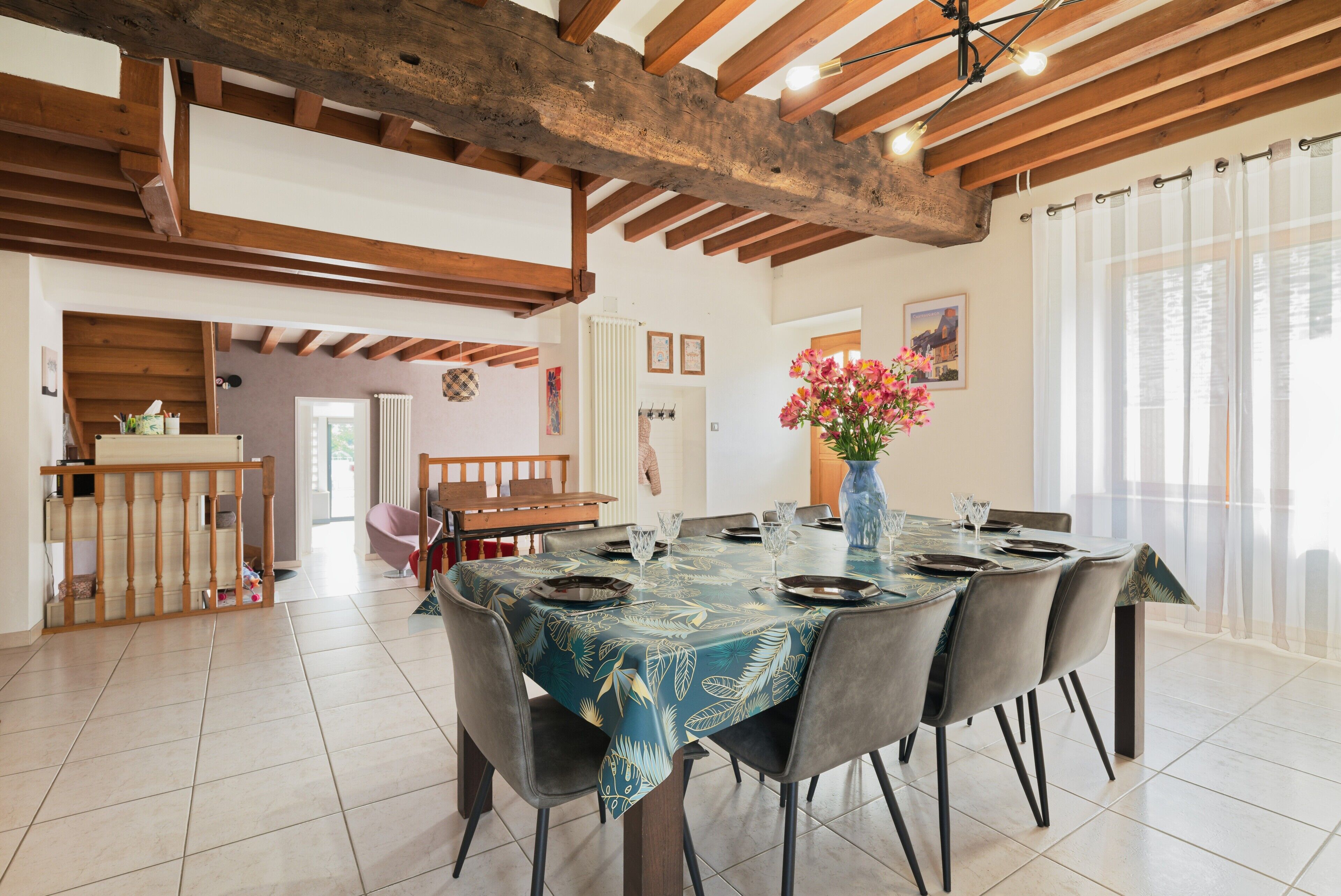 A dining area with a large table, chairs, and a vase with flowers.