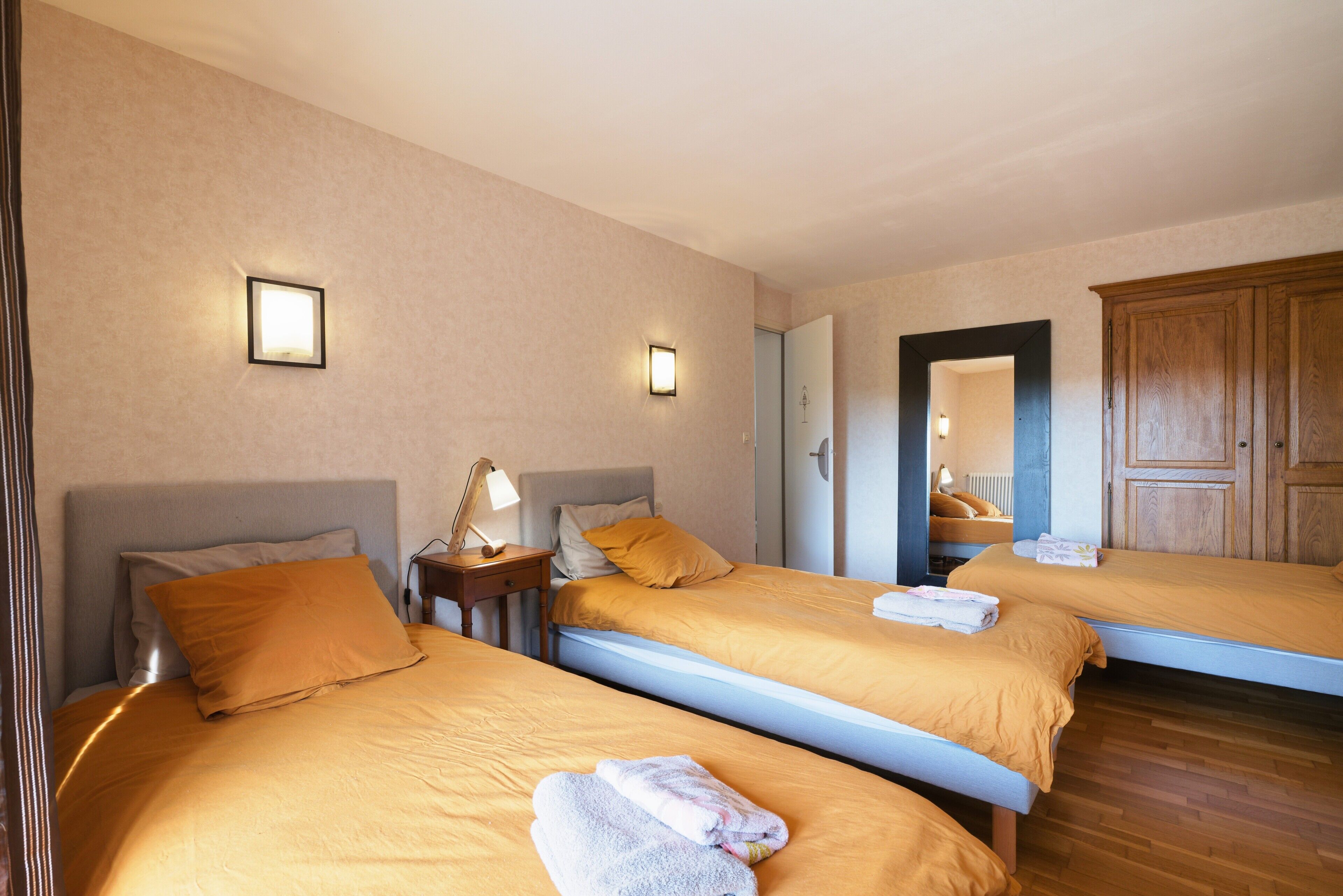 Ein Hotelzimmer mit drei Betten, einem Holzschrank und Nachttischlampen.