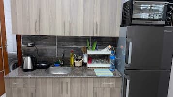 Een koelkast, een oven, een kookplaat, kookgerei, borden en bestek