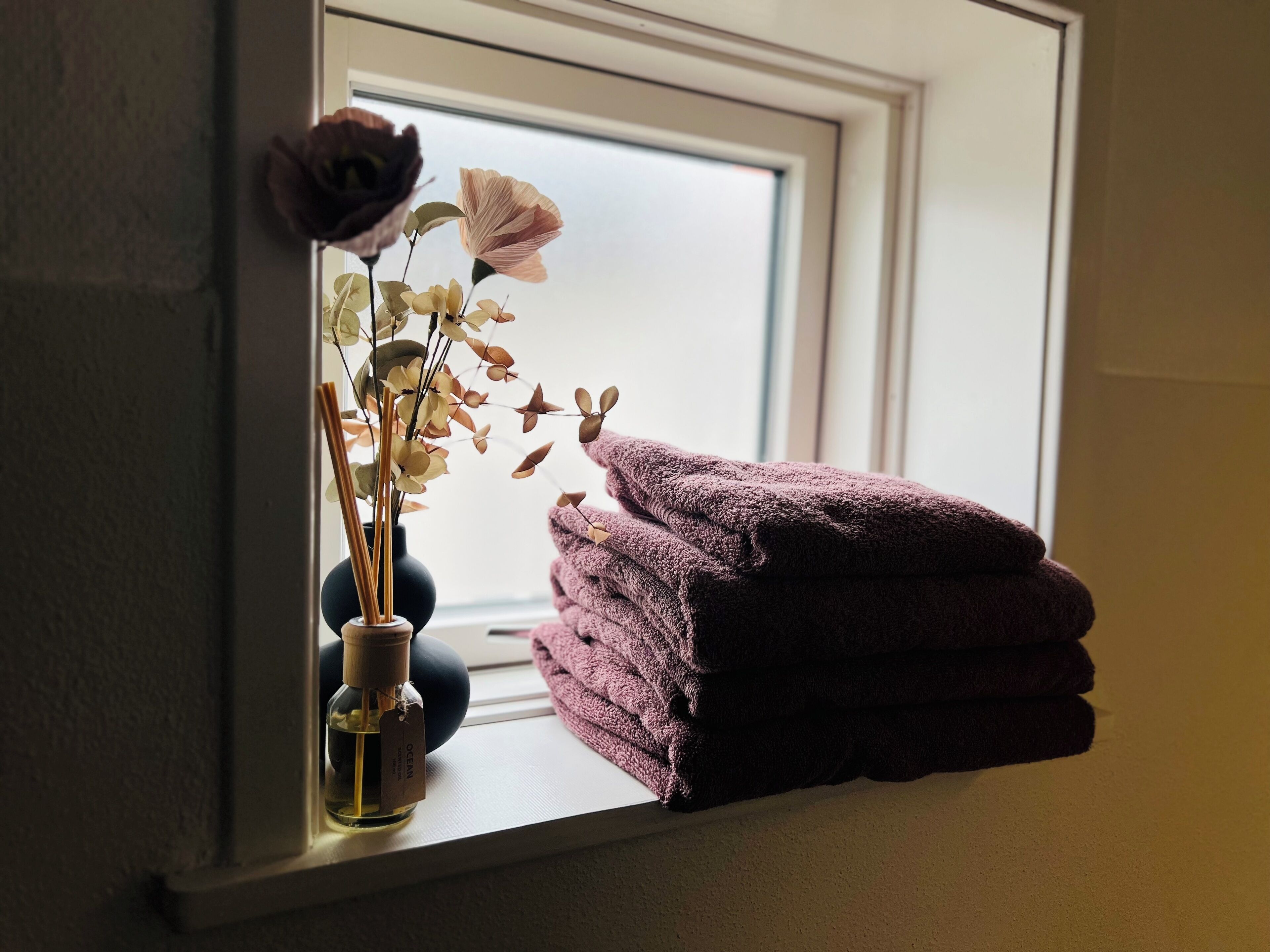 A window sill with a vase of dried flowers and a stack of towels.