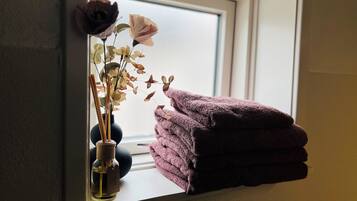 A window sill with a vase of dried flowers and a stack of towels.