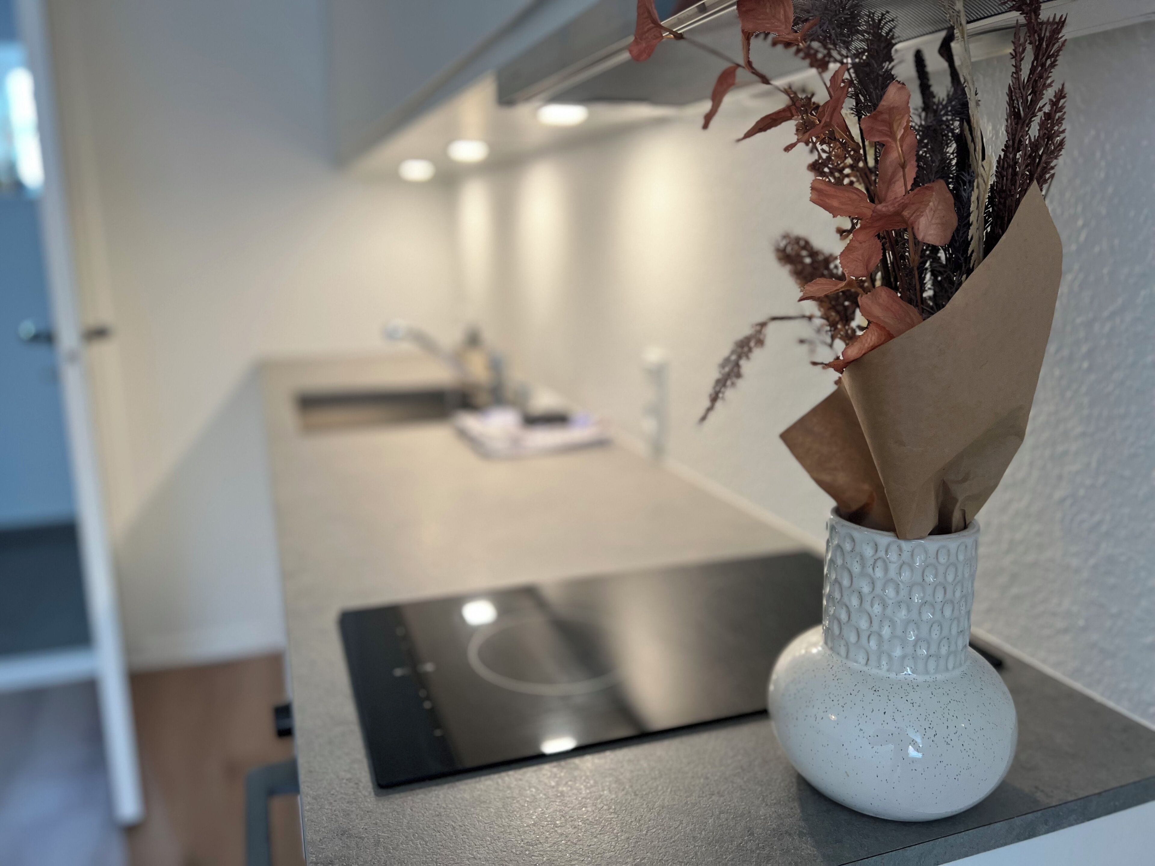 A kitchen counter with a white vase containing dried flowers and a paper bag.