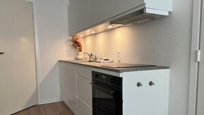 A compact kitchen with white cabinetry, a built-in oven, and a stainless steel range hood. - Cozy Flats Silkeborg - S1 (Silkeborg)
