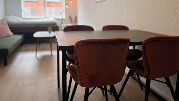 A dining area with a table and four chairs, a sofa, and a small table with a lamp. - Cozy Flats Silkeborg - S1 (Silkeborg)