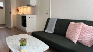 A modern kitchen with white cabinetry and a built-in oven, a dark green sofa with pink pillows, and a small round table with a plant. - Cozy Flats Silkeborg - S1 (Silkeborg)