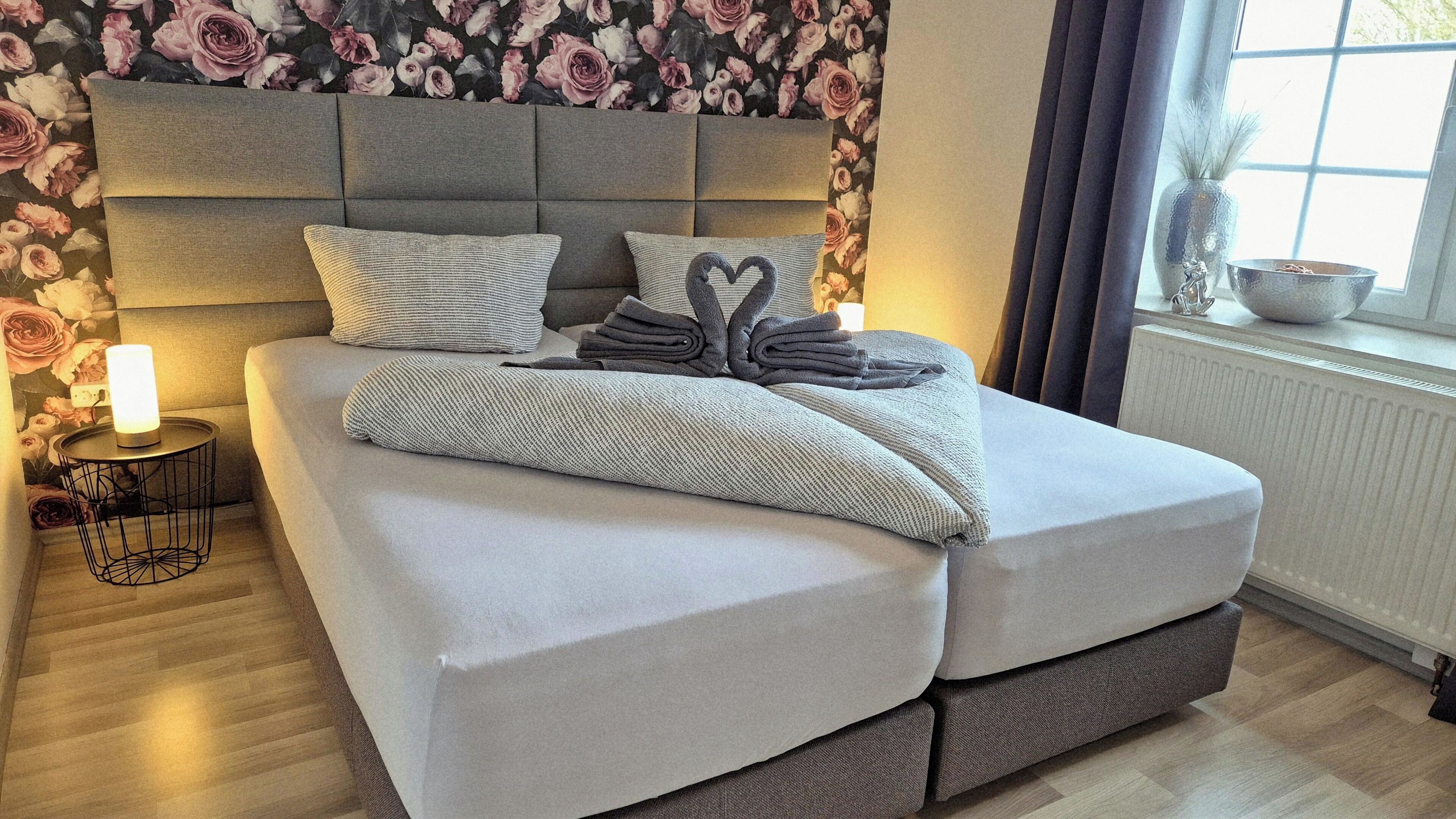 Une chambre moderne avec un lit, une table de chevet dotée d’une lampe et un papier peint à motifs floraux.