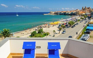 Un hotel frente al mar con vista a la playa, zona de estacionamiento y una calle con coches.