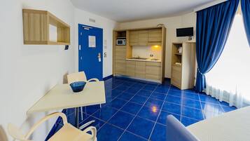 Una habitación de hotel compacta con kitchenette, piso de azulejos azules, una pequeña mesa de comedor y una sola silla.