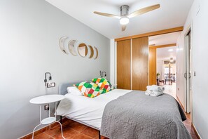 A bedroom with a bed, a ceiling fan, a bedside table, a wall-mounted power outlet, and a wooden wardrobe.