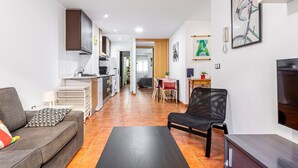 A modern living room with a sofa, a black chair, a TV, and a kitchen in the background. - Apartment 'Torres De Quart Tu Casa' with Balcony, Wi-Fi and Air Conditioning (València)
