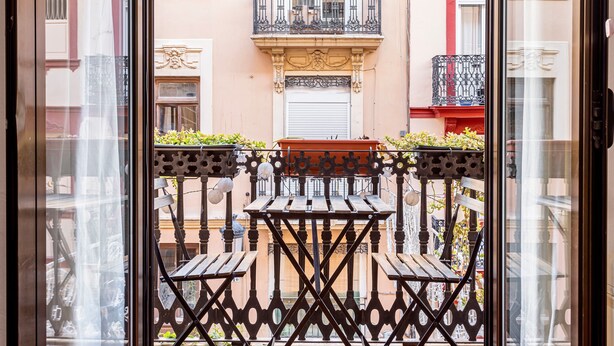 A balcony with a wooden table and chairs, a potted plant, and a decorative railing. - Apartment 'Torres De Quart Tu Casa' with Balcony, Wi-Fi and Air Conditioning (València)