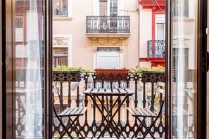 Un balcón con una mesa y sillas de madera, una planta en maceta y una barandilla decorativa.