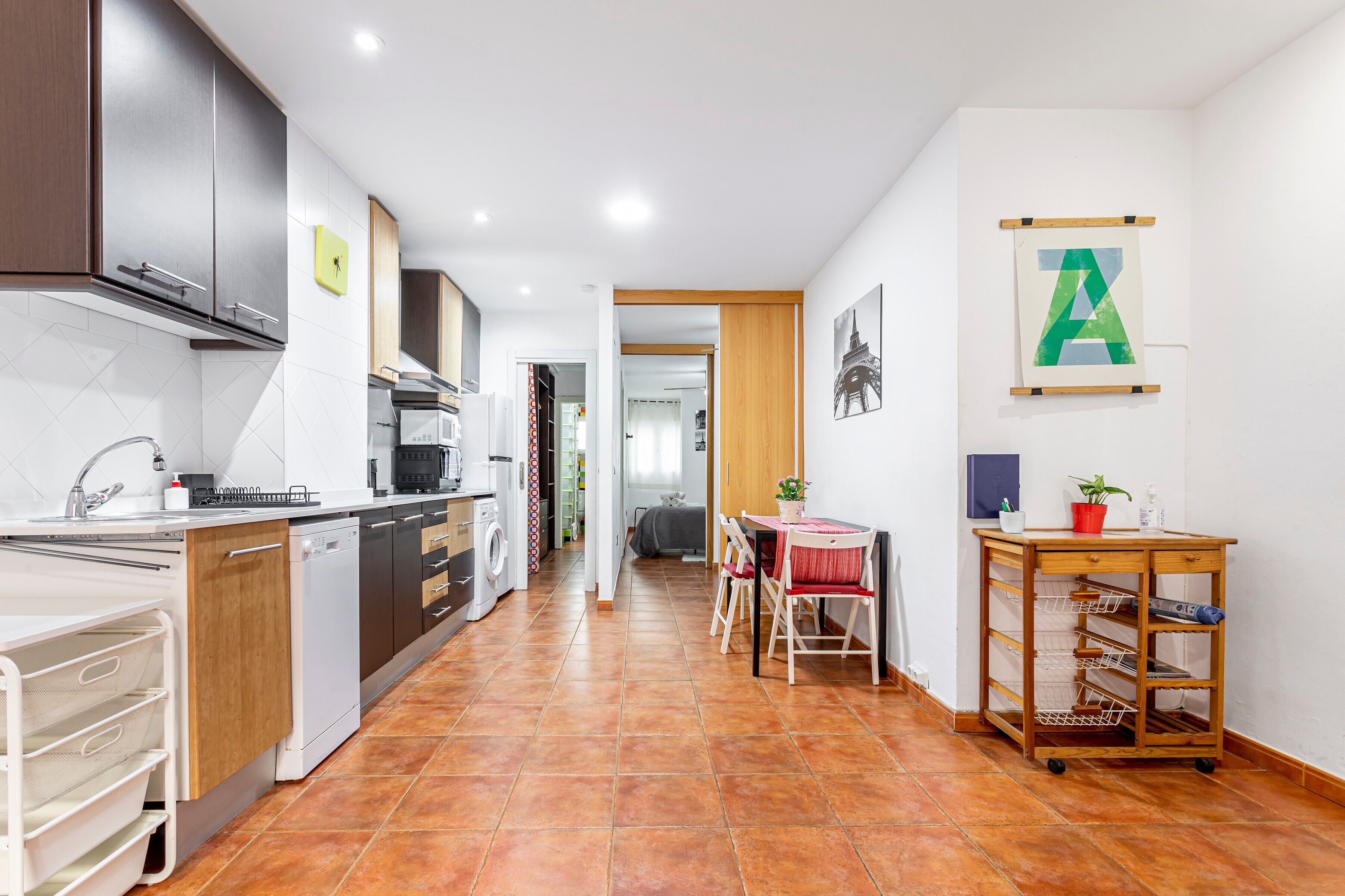 Een moderne keuken met een vaatwasser, oven en kastjes. Er is een eethoek met een tafel en stoelen.