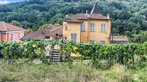 A yellow building with a red-tiled roof, surrounded by greenery and a mountainous backdrop.