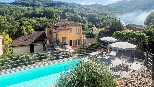 A poolside area with lounge chairs and a swimming pool, surrounded by a fence and greenery.