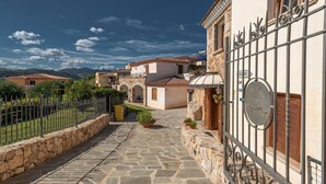 A stone-paved courtyard with a metal gate, a stone wall, and a building with a tiled roof. - Residence in Budoni with 1 bedrooms sleeps 4 (Budoni)