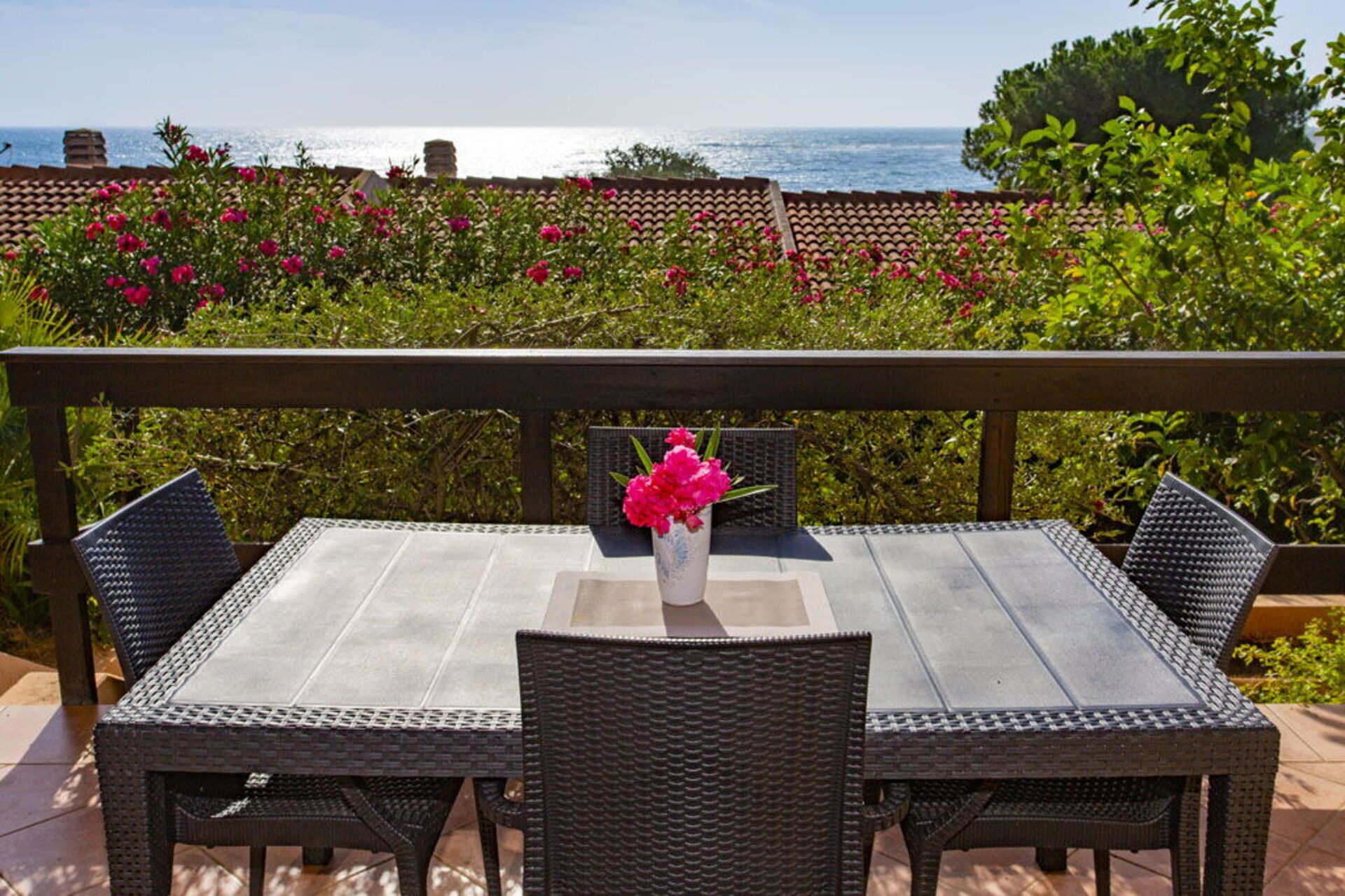 En terrasse med et bord og stole, en vase med blomster, og udsigt til havet.