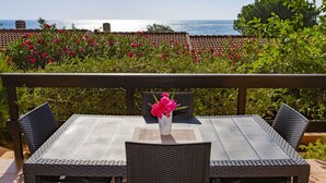 Une terrasse avec une table et des chaises, un vase rempli de fleurs et une vue sur la mer.