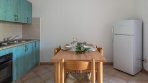 Une cuisine compacte avec des meubles de couleur turquoise, un réfrigérateur blanc et une table à manger en bois, préparée pour deux personnes.