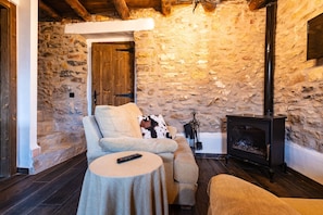 A stone-walled room with a sofa, a round table, a remote control, and a fireplace.