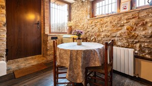 Habitación de paredes de piedra con puerta de madera, una mesa redonda con sillas, un radiador y una ventana con vistas.