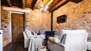 Una habitación rústica con paredes de piedra, chimenea, dos sofás, una mesita y televisor montado en la pared.