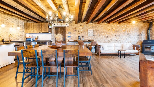Eine rustikale Küche mit einem Holztisch, blauen Stühlen, einer Steinwand und einem Kamin.