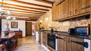 Een keuken met houten kastjes, een stenen muur en een houten eettafel met stoelen.
