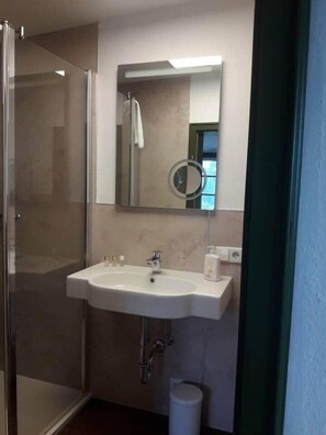 Un baño con cabina de ducha de vidrio, un lavabo blanco con espejo y un inodoro.