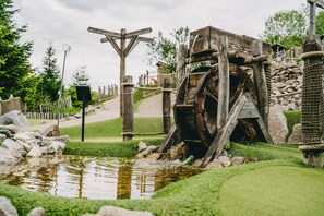 Una rueda hidráulica en un parque con una estructura de madera, un estanque pequeño y una valla.