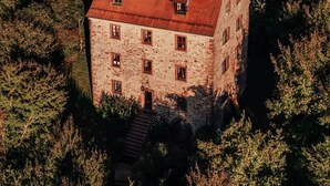 Un edificio de piedra con techo rojo, rodeado de árboles y líneas eléctricas al fondo.