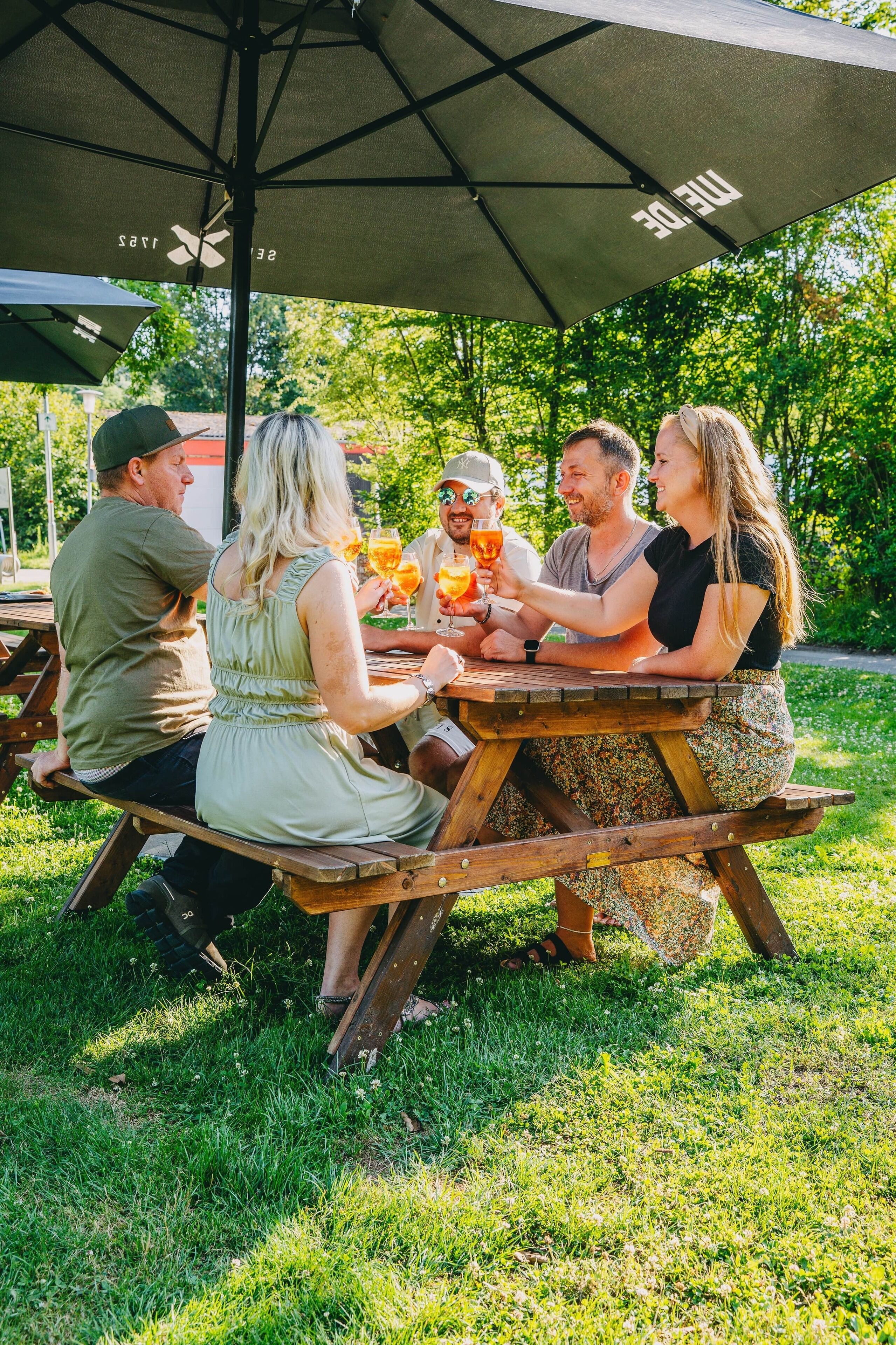 A group of people sitting at a wooden picnic table under a large umbrella.