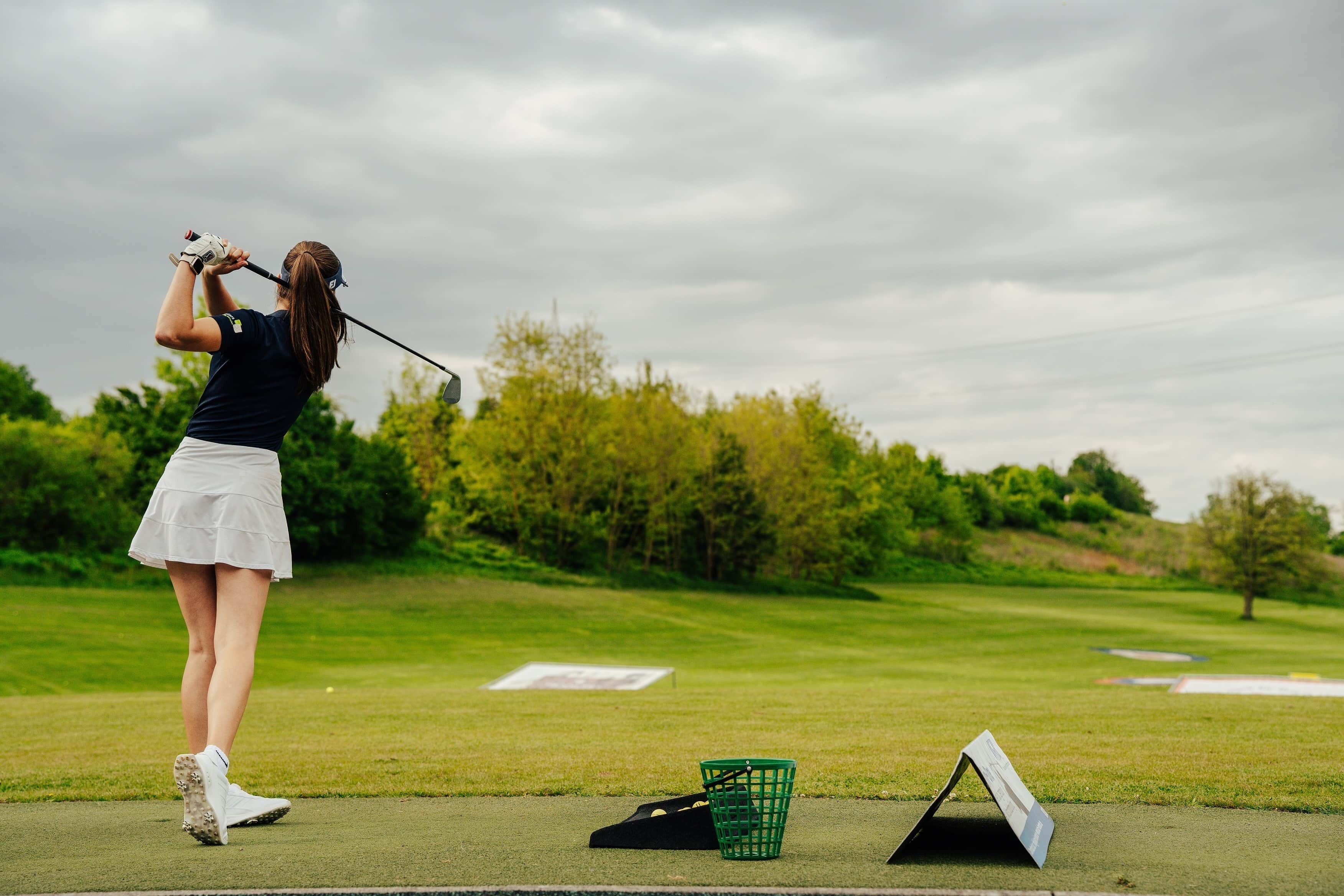 A person playing golf on a course with a green basket and a white tee box visible.