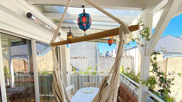 A hammock chair suspended from a ceiling, a table with a cushion, and a view of the outside through a glass door. - Absolute peace and terrace in Bastille (Paris)