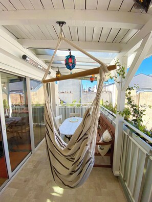 A hammock chair suspended from a ceiling, a table with a cushion, and a view of the outside through a glass door. - Complete tranquility and a terrace in Bastille (Paris)