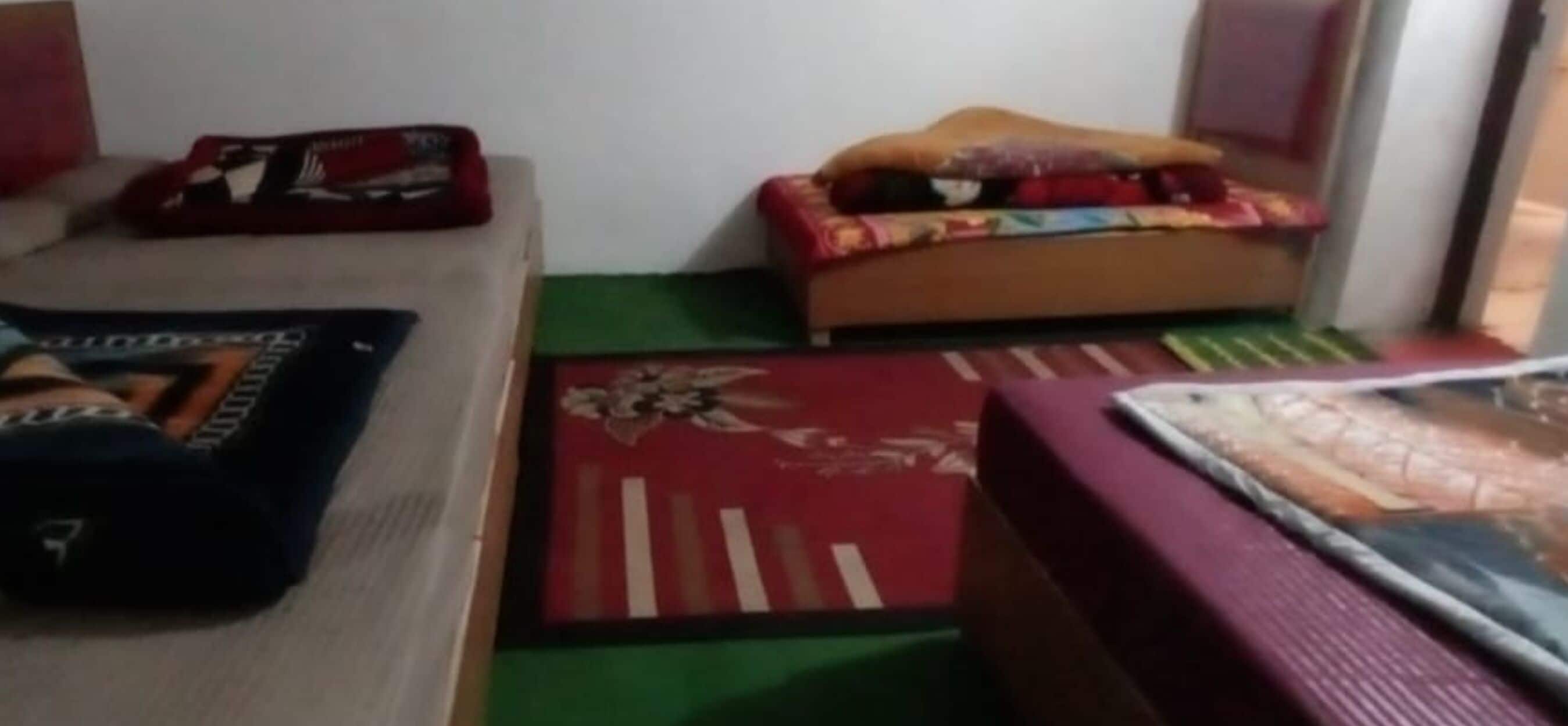 A room with a bed, a small sofa, and a table. There are two rugs on the floor.