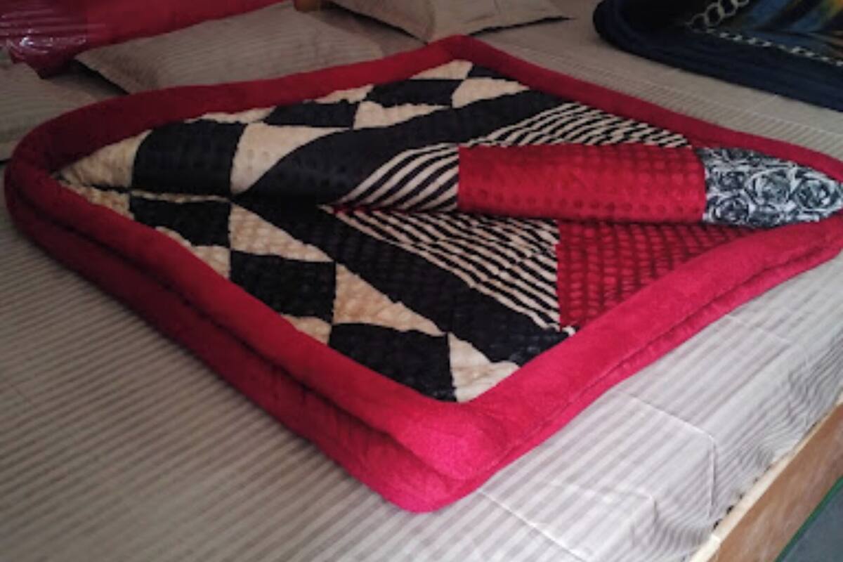 Ein Bett mit einer rot-schwarzen Steppdecke, einem Holz-Kopfschild und einem grünen Teppich.