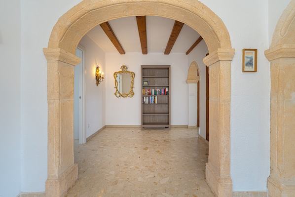 An arched hallway with a tiled floor, a bookshelf, and a framed picture on the wall.