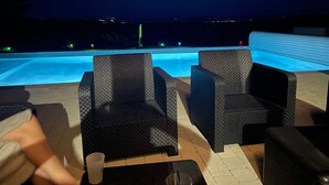 Un espace aménagé au bord de la piscine, avec des meubles en osier et une vue sur la piscine la nuit.