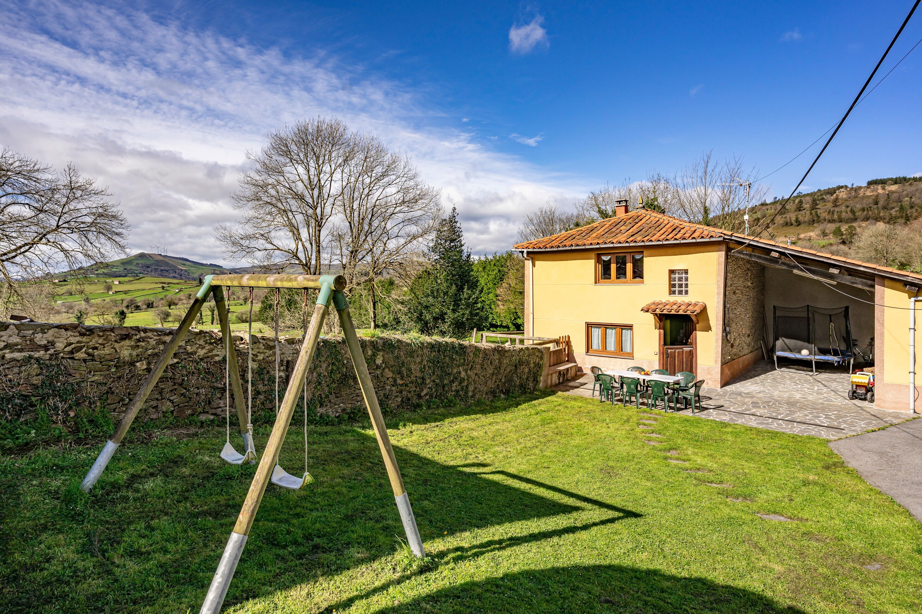 A house with a patio, a swing set, and a stone wall.
