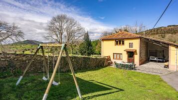A house with a patio, a swing set, and a stone wall.