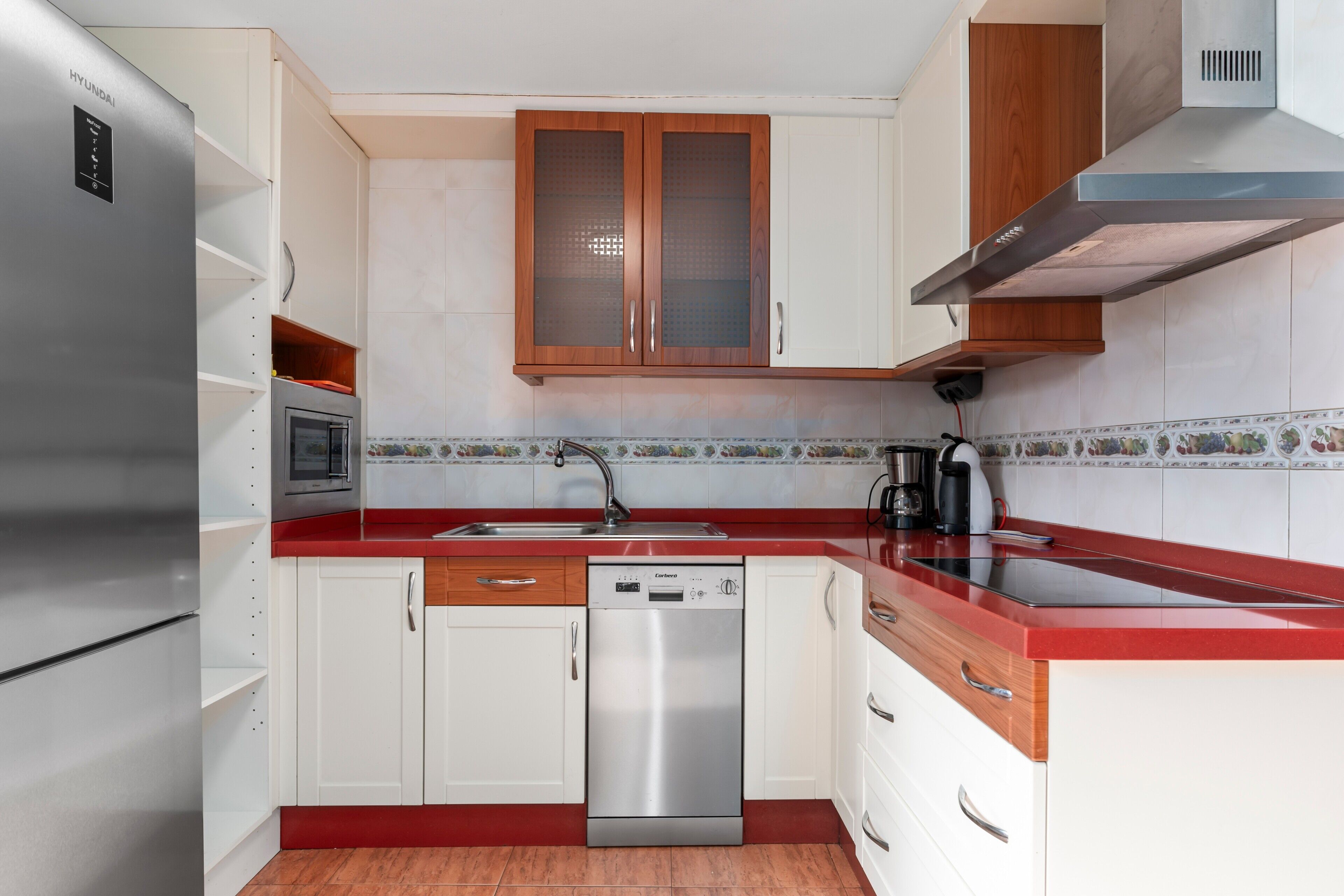 Una cocina moderna con armarios blancos, un lavavajillas de acero inoxidable y una encimera roja.