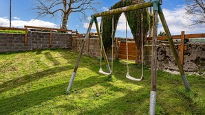 Une balançoire installée dans une cour verdoyante, avec un mur de briques et une clôture en bois.
